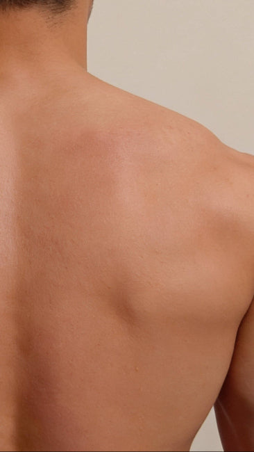 Rear view of a man's bare back showing his shoulders, upper back, and spine against a plain beige background.